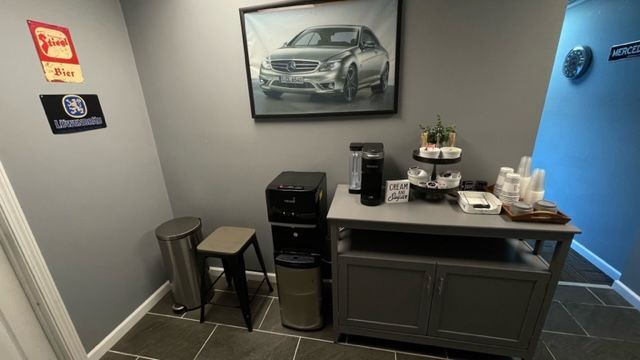 A coffee station in a gray-walled room with a Mercedes Benz photo and a small stool. | Benz Tech