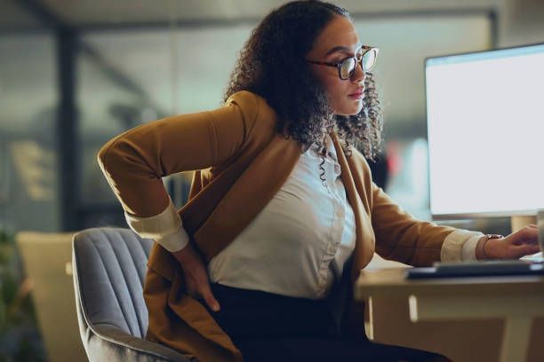 A woman is sitting at a desk with her hands on her back.
