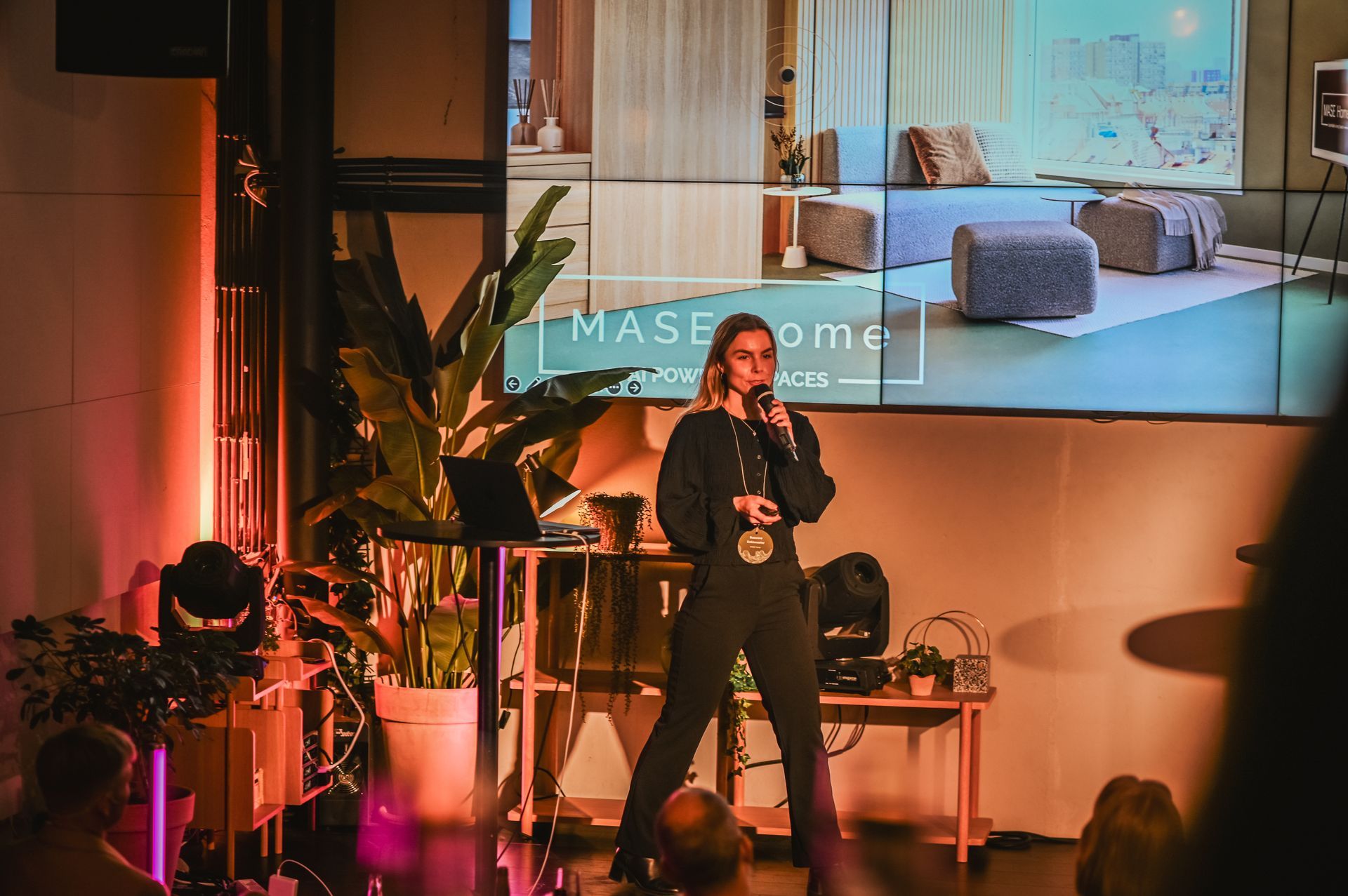Woman in blue dress and man in blue suit on stage, smiling and presenting.