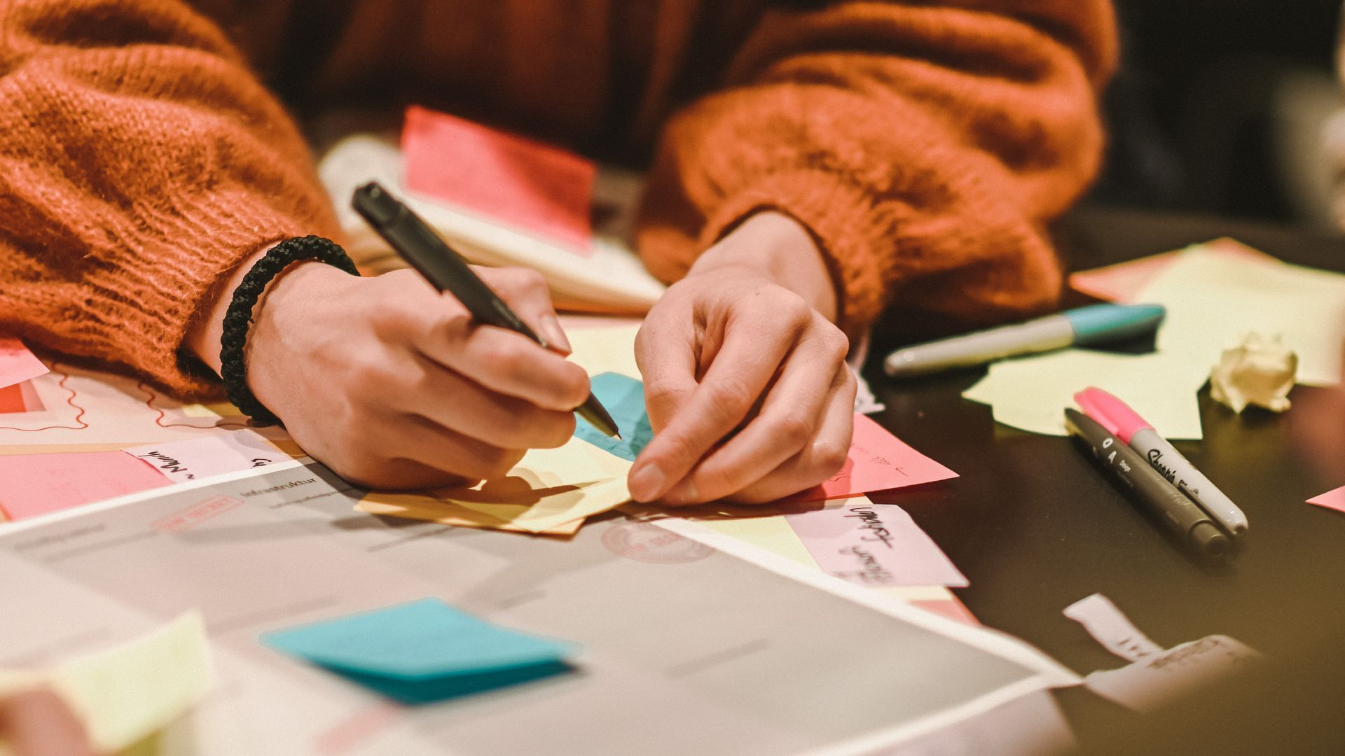 People in business attire at a table, discussing. Woman in white sweater looks up; German flag present.