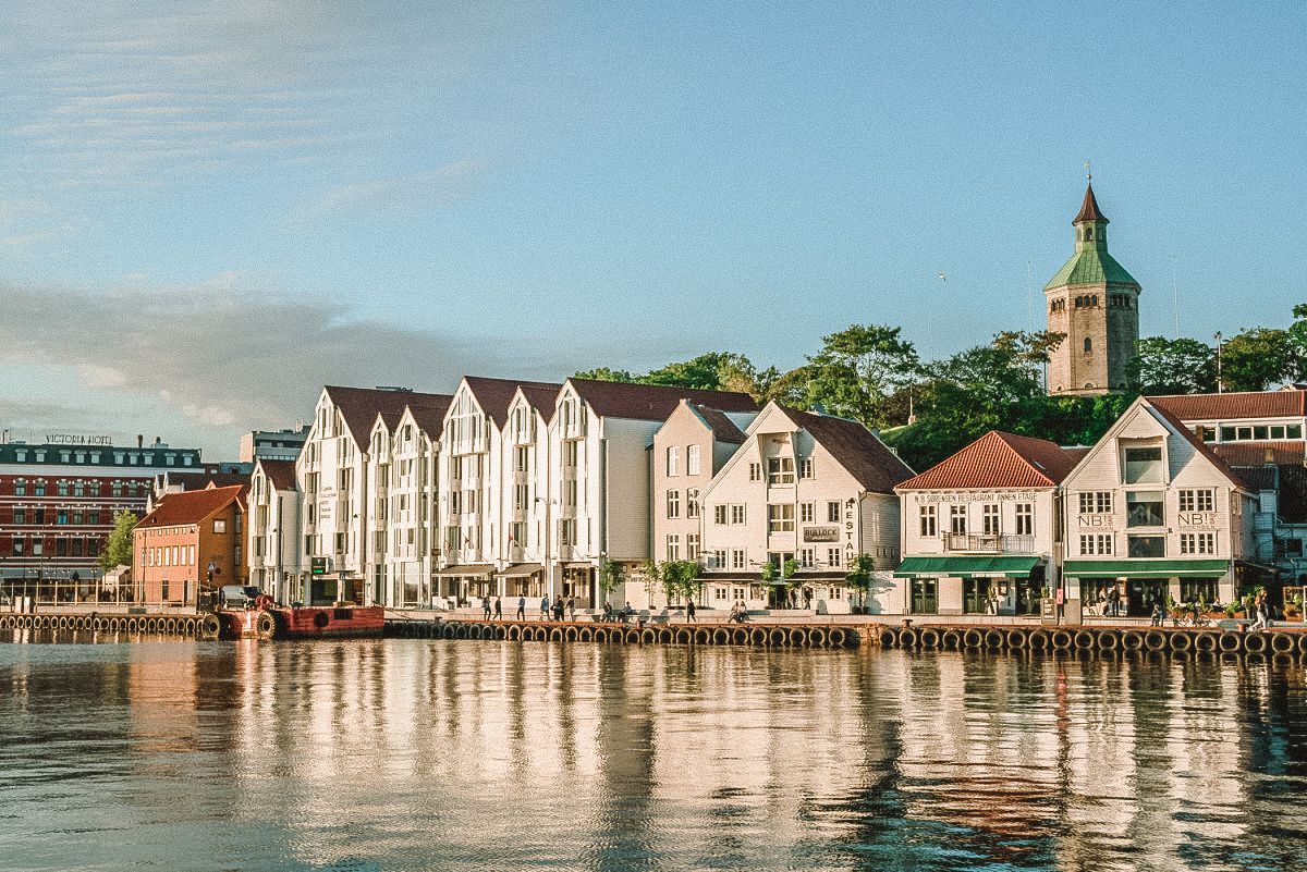 Waterfront cityscape with white buildings, red roofs, a church tower, and a calm body of water.