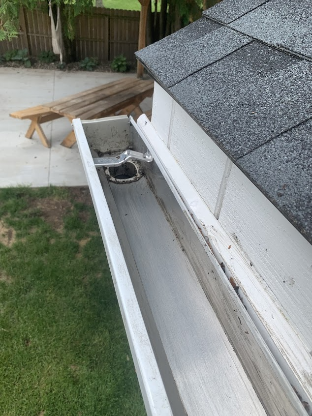 A gutter on the side of a house with a picnic table in the background.