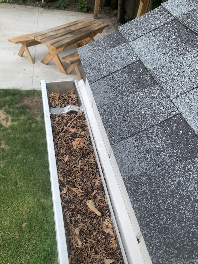 A gutter filled with leaves on a roof next to a picnic table.