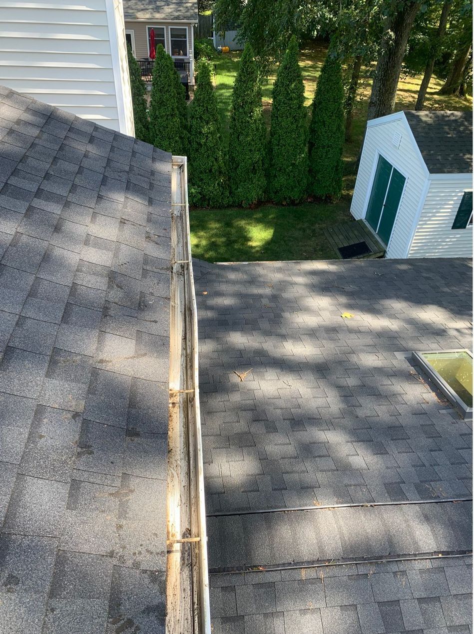 A roof with a gutter on it and a shed in the background.