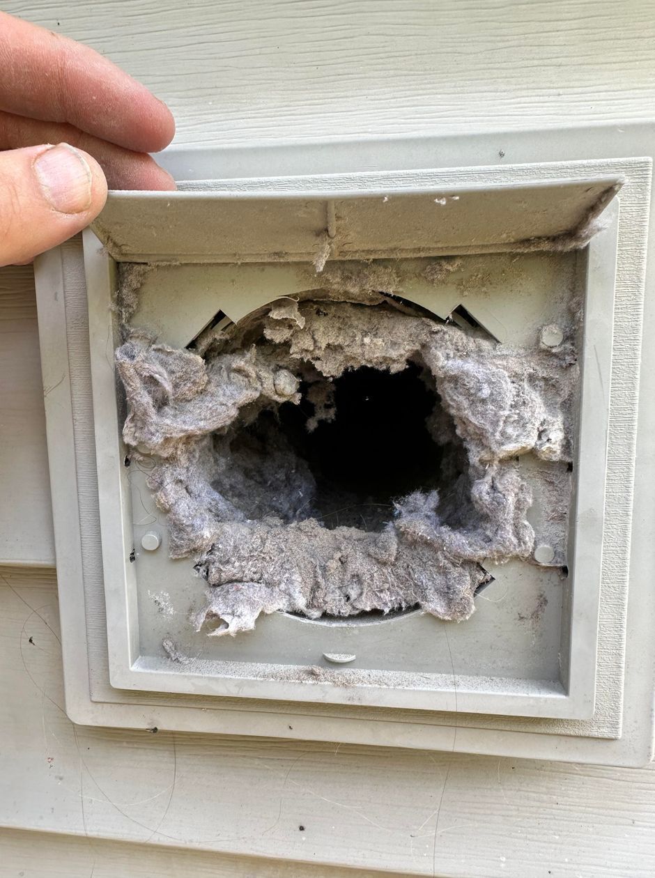 A person is holding a dirty vent on the side of a house.