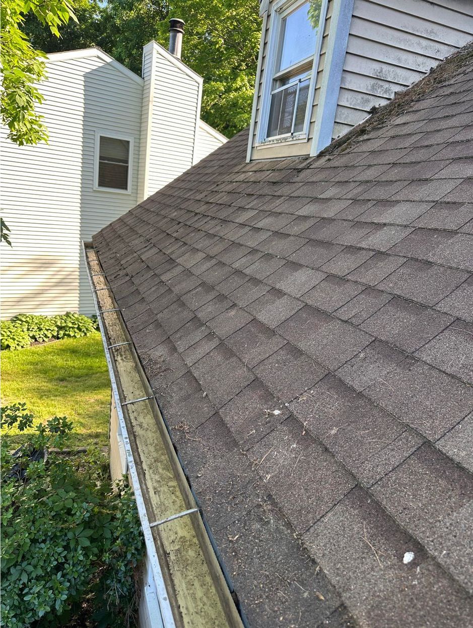 A close up of a roof with a gutter on it and a house in the background.