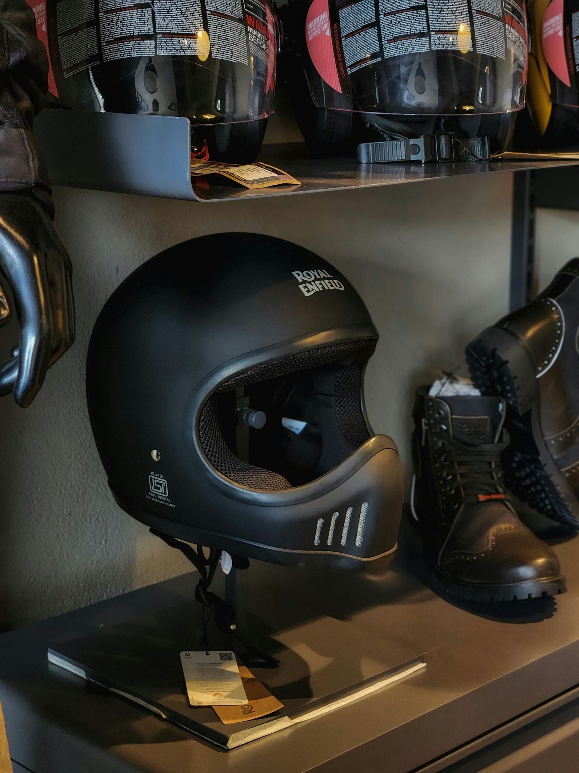 Black Royal Enfield motorcycle helmet displayed with boots on a shelf.