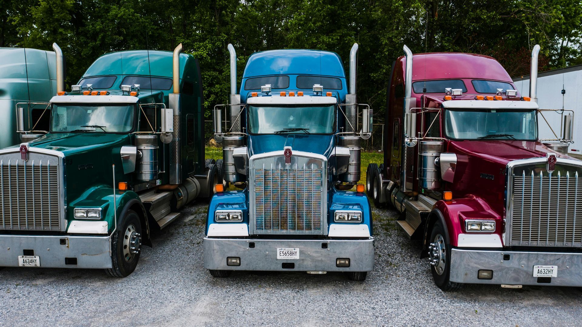 Three colorful semi-trucks parked in a row: green, blue, and red, facing forward.