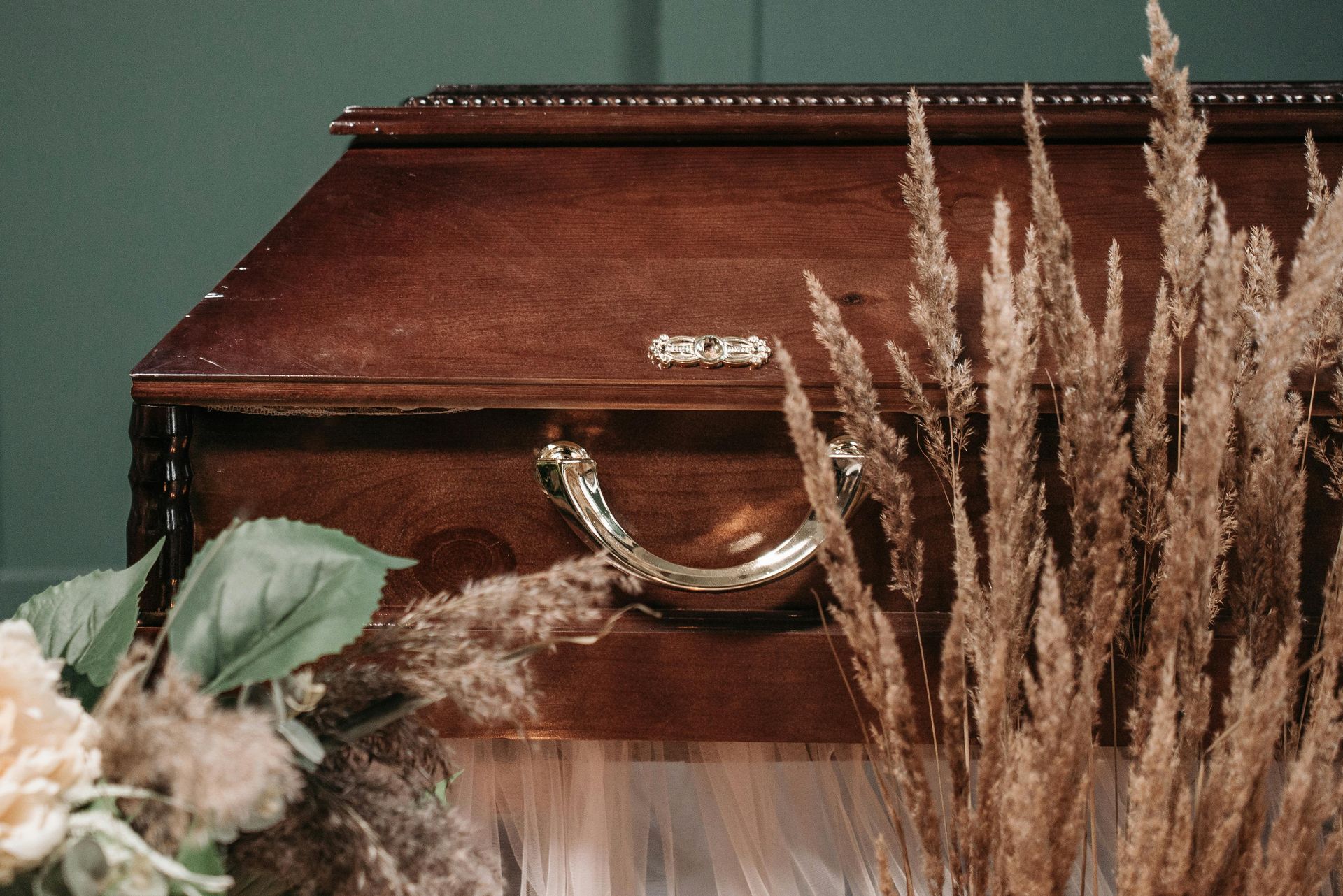 Wooden casket with gold handle, surrounded by dried wheat and flowers, in a dimly lit setting.