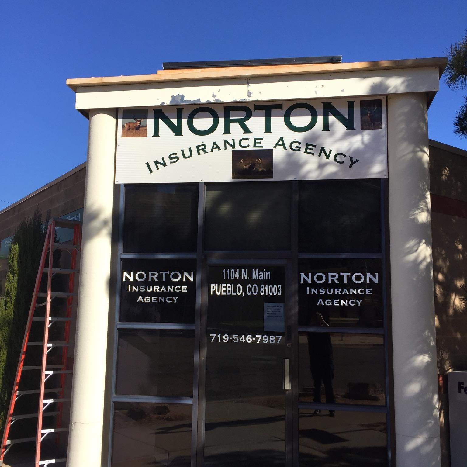 Norton Insurance Agency building with sign and glass door. A ladder is leaning against the building.