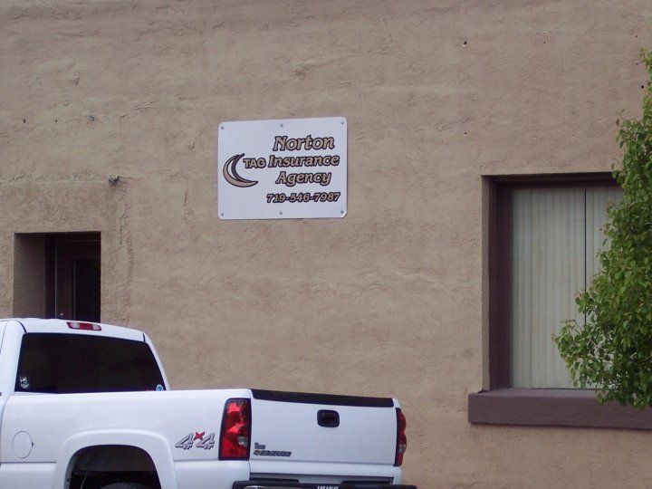 White pickup truck parked outside a building with sign for Norton Insurance Agency.