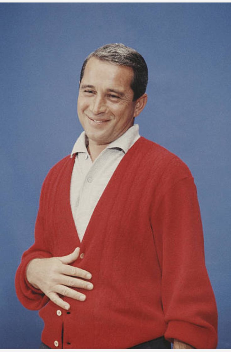 A person smiling while wearing a red cardigan over a collared shirt against a blue background.