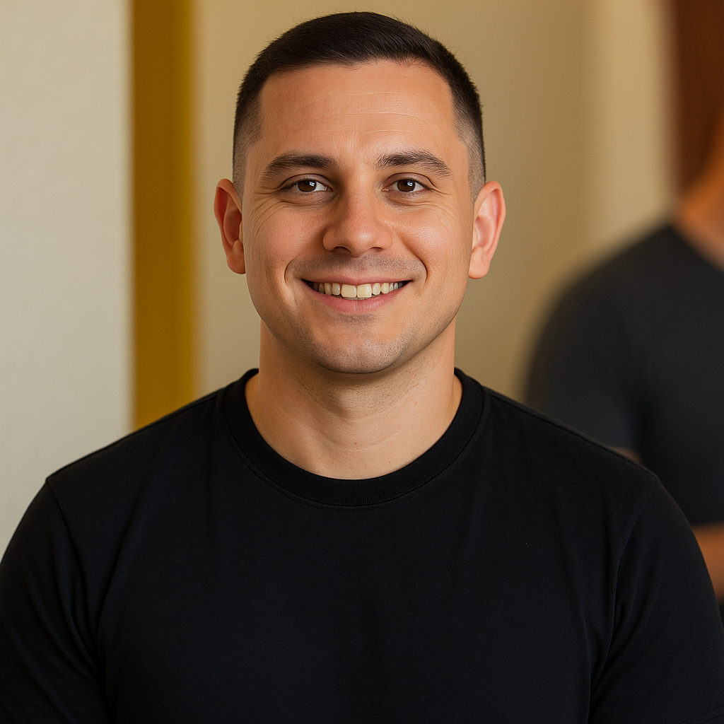 Man in black shirt smiling, indoors with neutral background.
