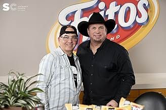 Two people standing in front of a Fritos logo sign indoors, with a plant in the foreground and snacks on a table.