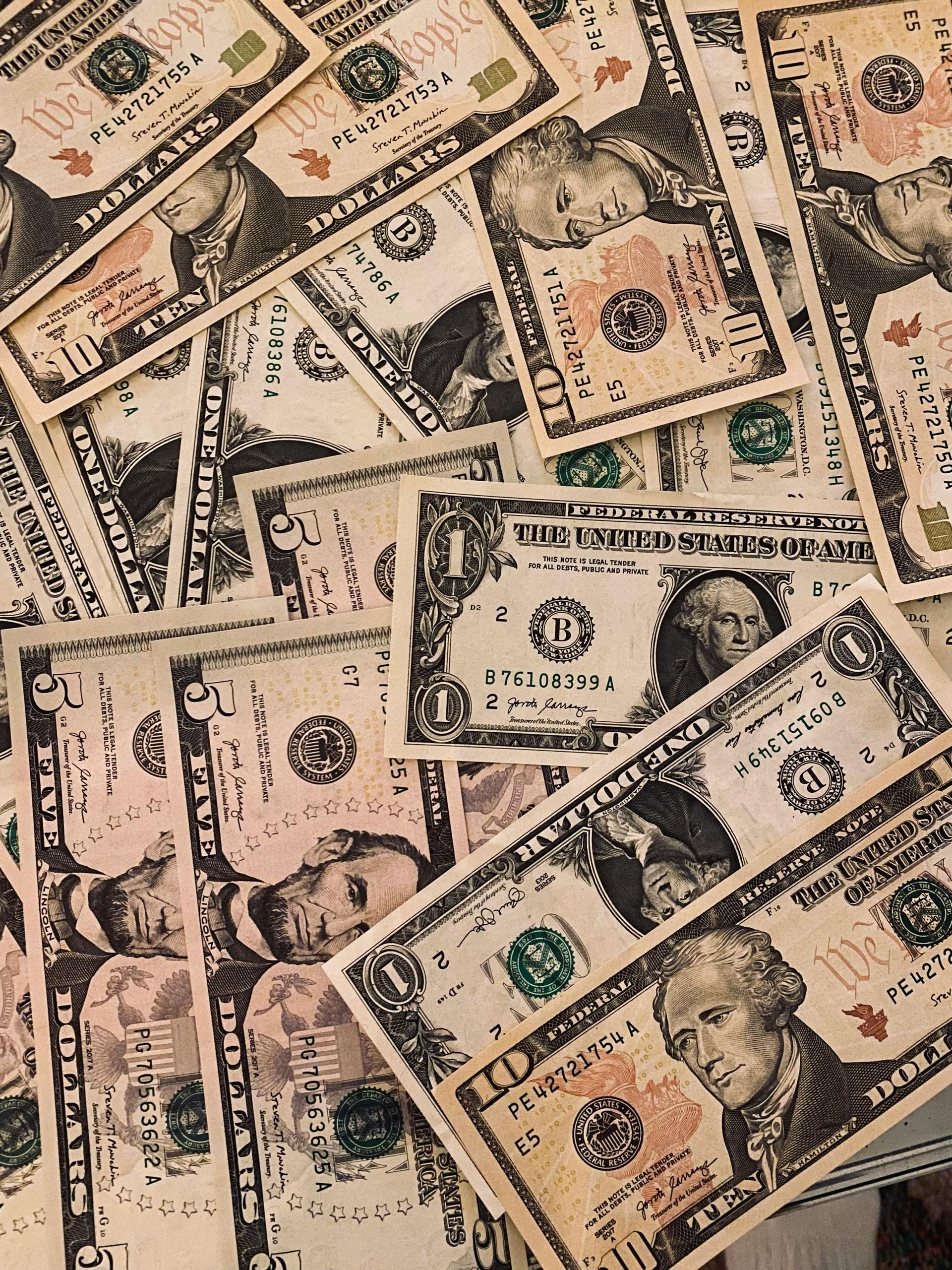 A scattered pile of assorted U.S. dollar bills, including five and ten dollar denominations.