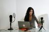A woman is sitting at a table with a laptop and two microphones.