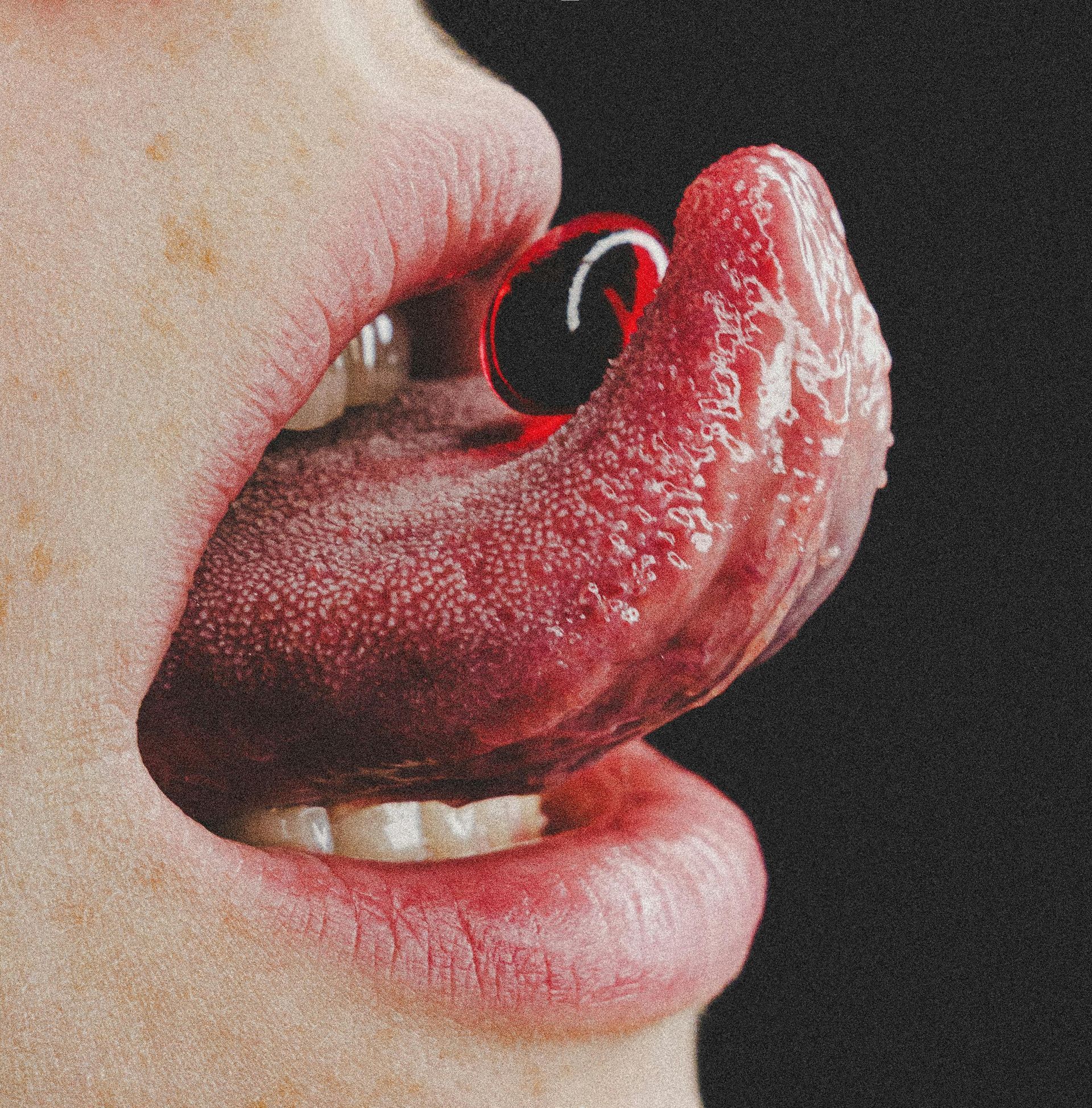 Close-up of an open mouth with a textured tongue holding a glossy, oval-shaped red pill against a black background.
