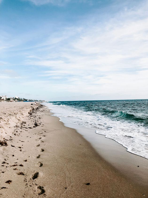 Sandy beach with waves crashing. Sky is blue with light clouds.