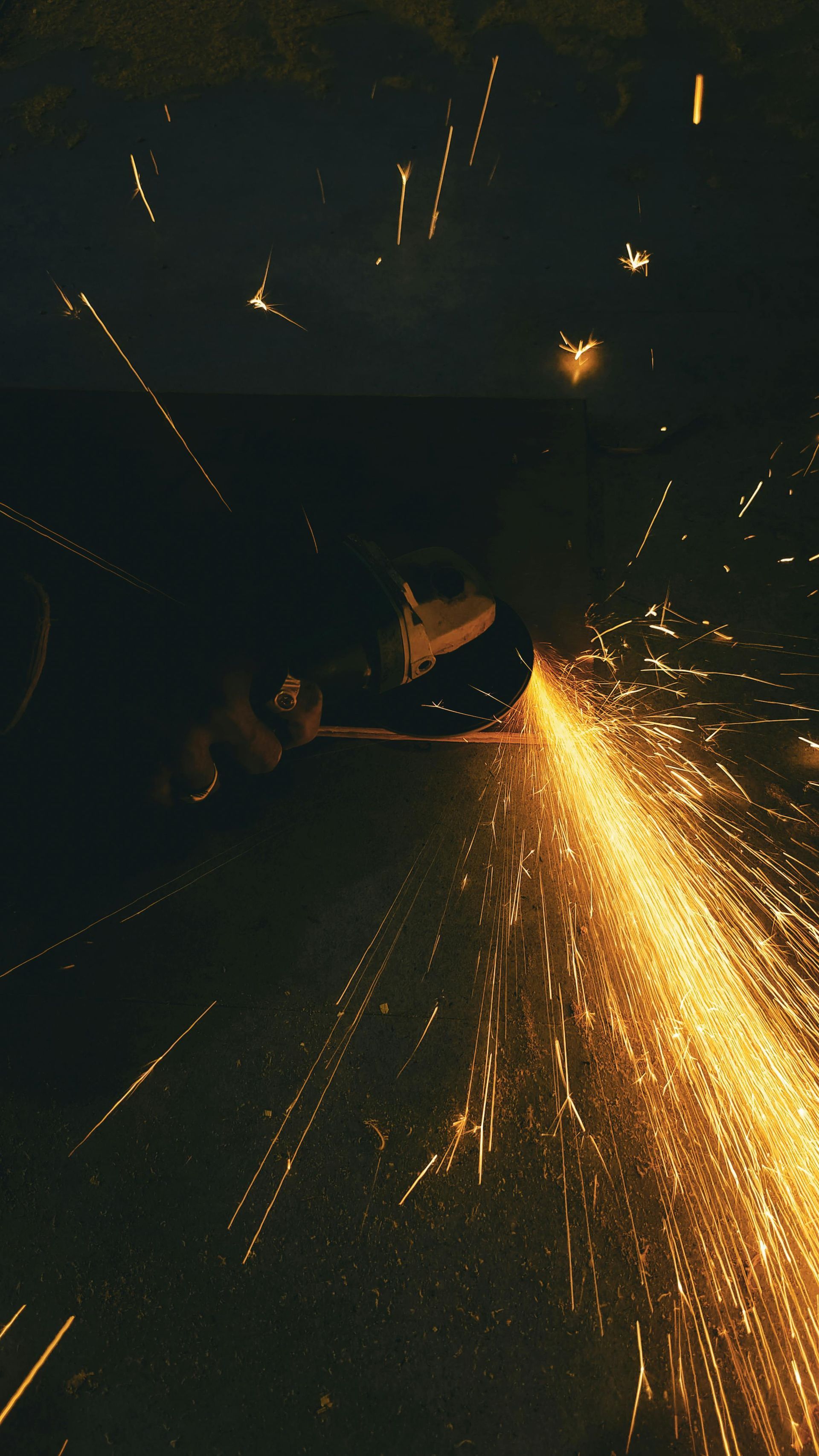 A hand using an angle grinder on metal, creating a brilliant, glowing fan of bright orange sparks in the dark.