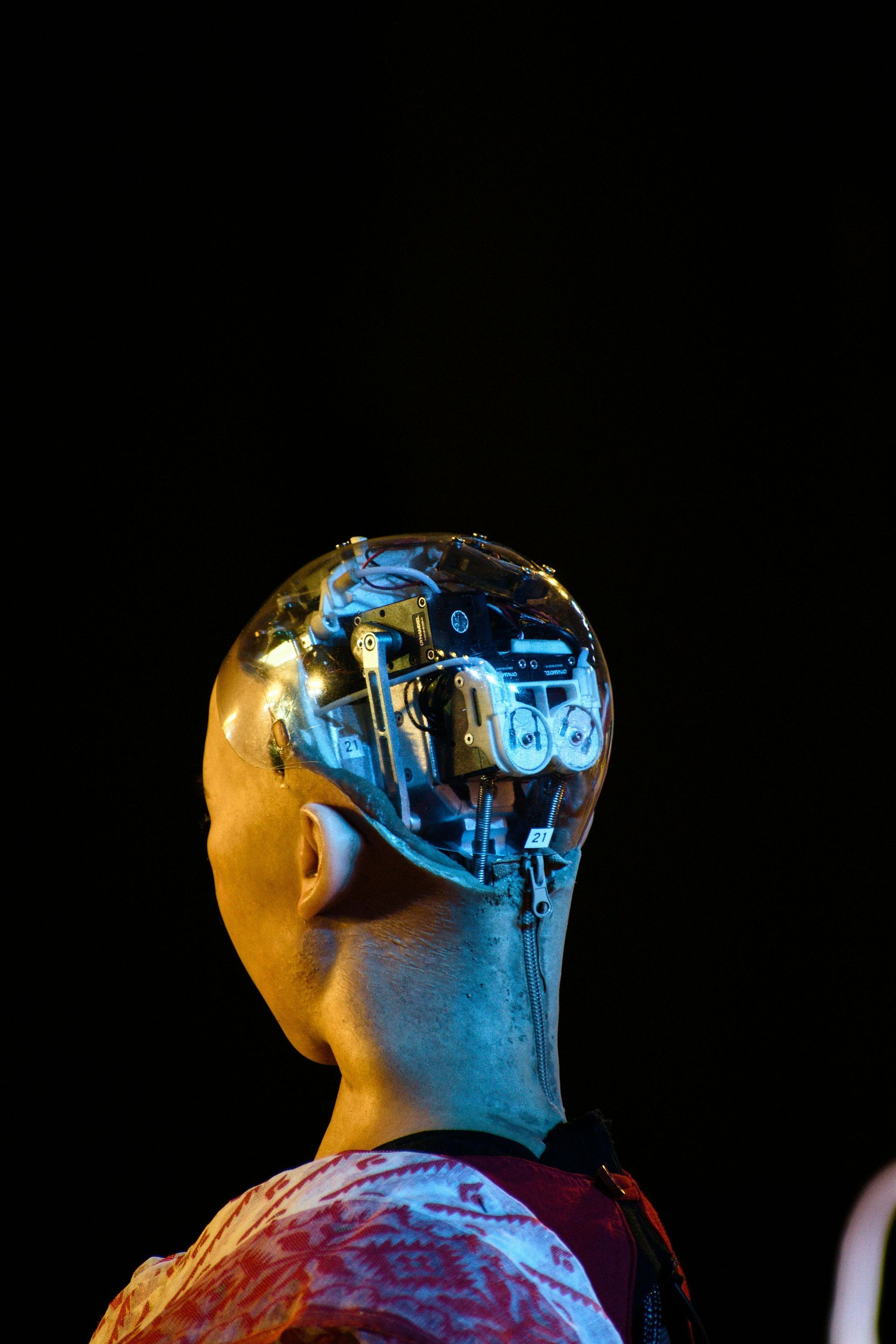 A humanoid figure with a transparent skull revealing intricate mechanical components against a dark background.