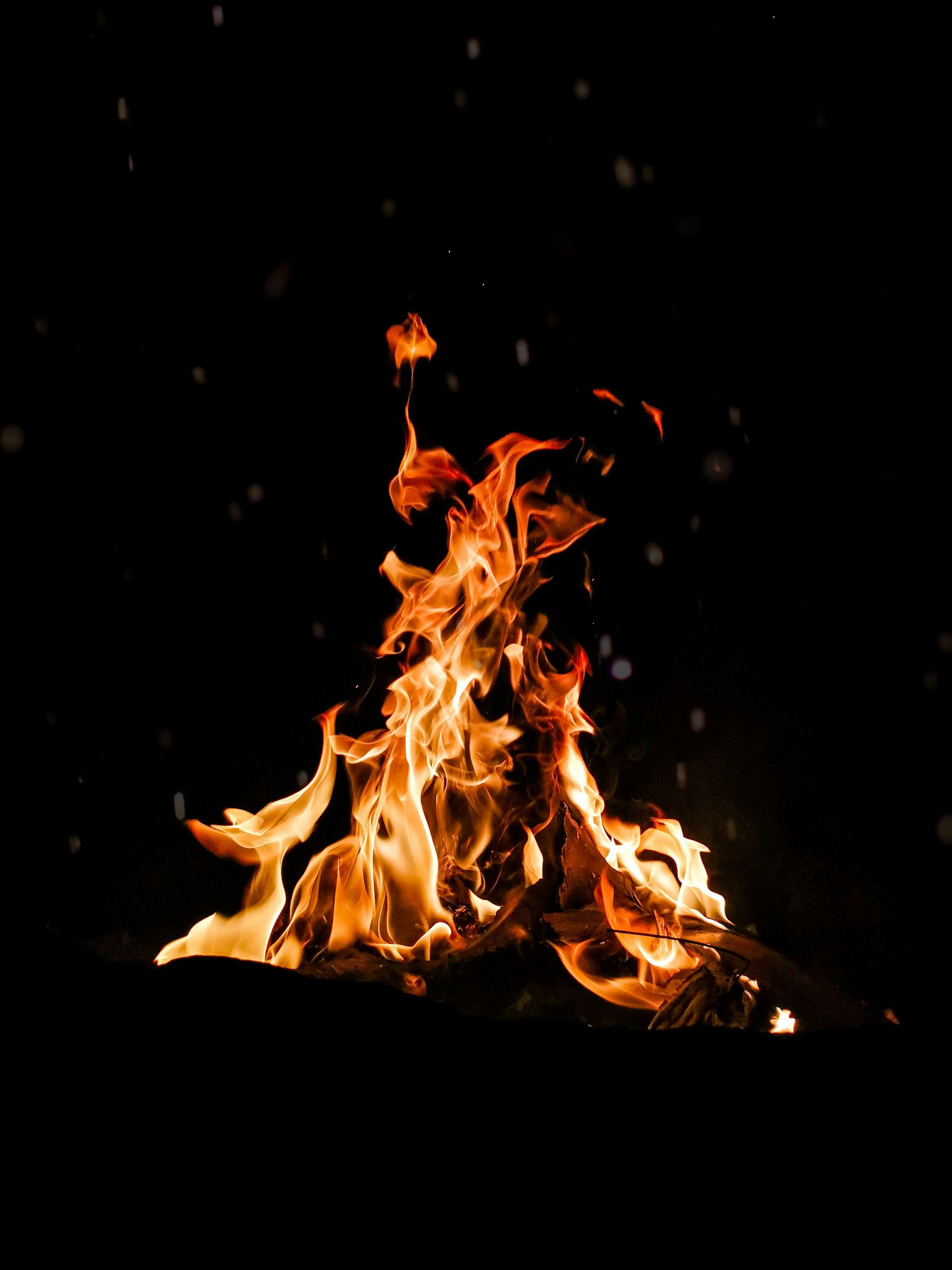 A bright, flickering bonfire burns against a dark, night background with scattered embers.