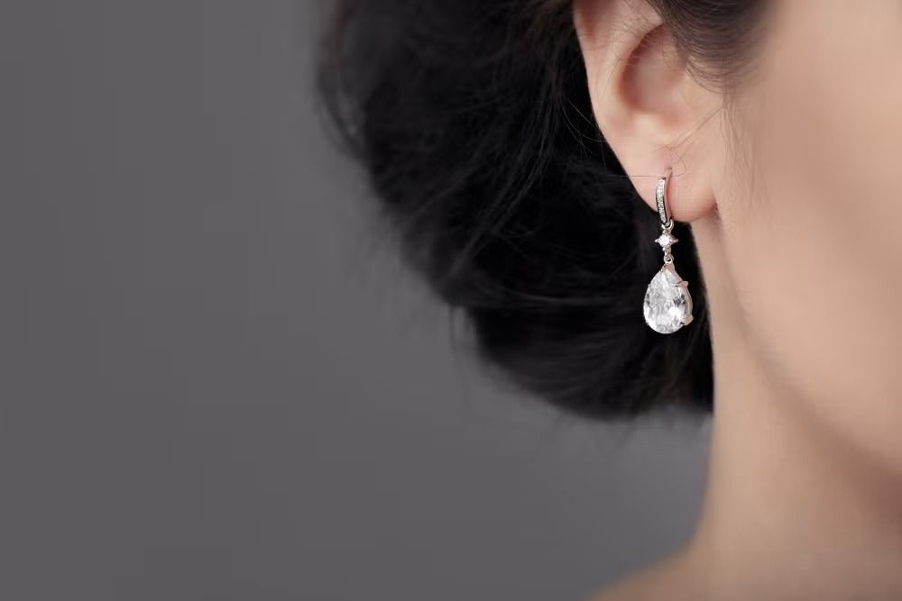 Close-up of a person wearing a pearl drop earring against a gray background