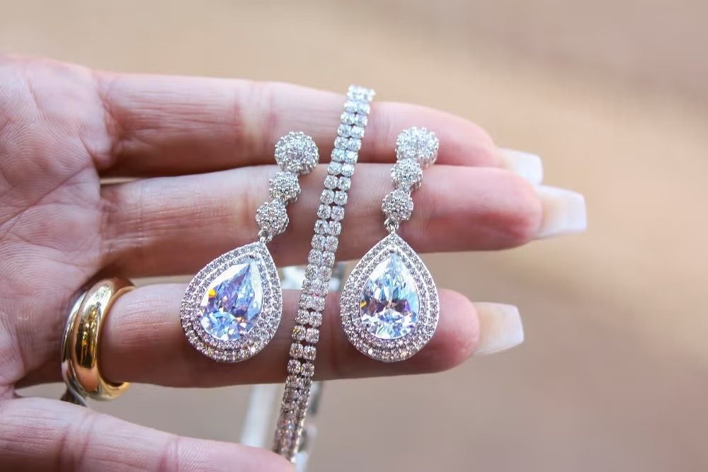 Hand holding silver teardrop earrings and bracelet with sparkling clear stones