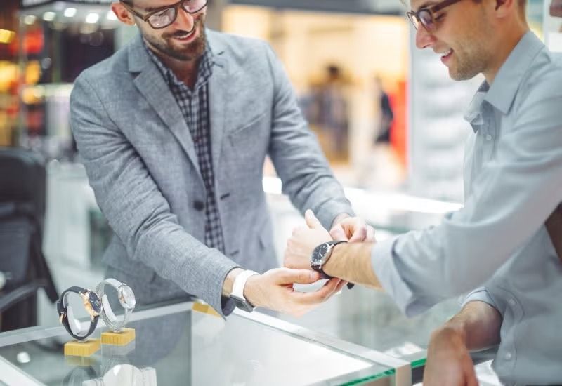 Two men in a jewelry store exchanging a watch over a glass display case