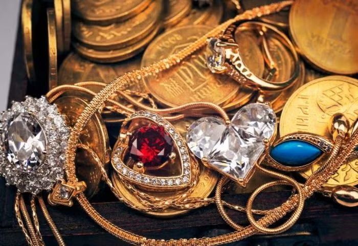 Gold jewelry with diamond and gemstone rings, including red and blue stones, on a dark surface