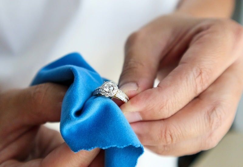 Hands hold a diamond ring tied with a bright blue ribbon
