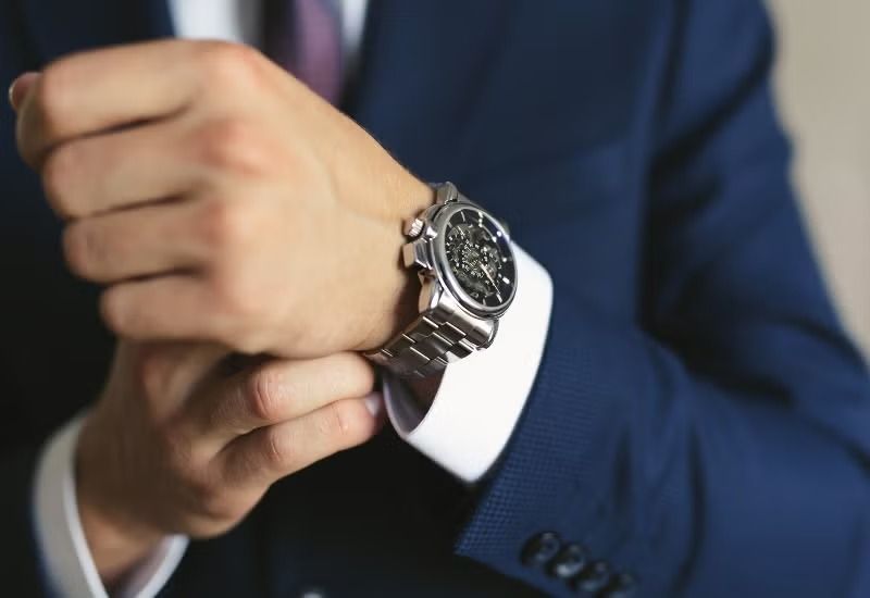 Close-up of hands adjusting a silver wristwatch with a dark suit and white cuff visible