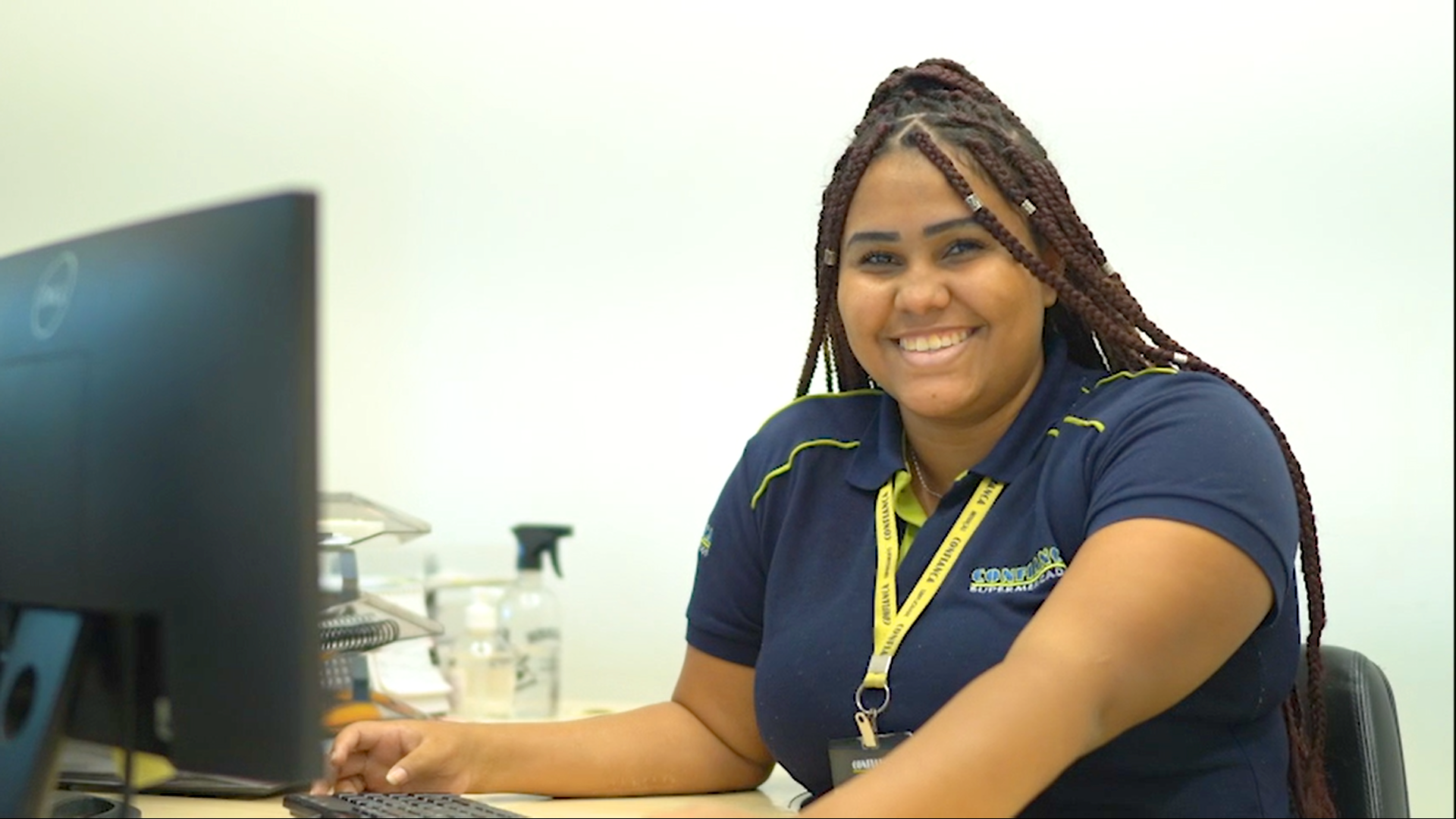 Uma mulher está sentada em uma mesa em frente a um computador e sorrindo.