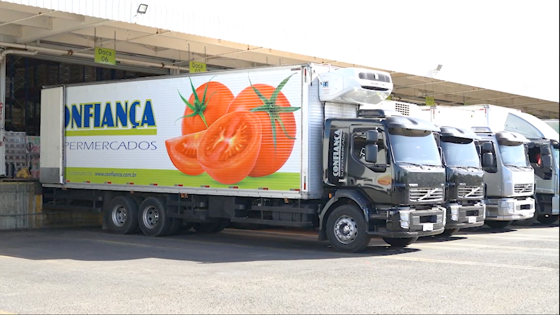 Uma fileira de caminhões está estacionada em um estacionamento e um deles tem uma foto de tomates na lateral