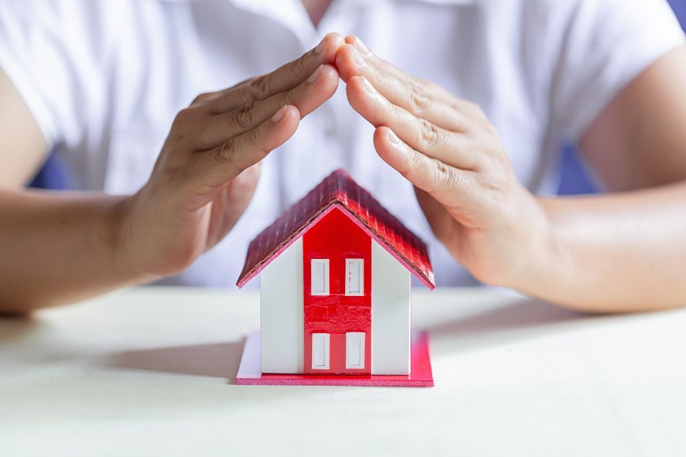 Hands cupped over a miniature house with a red roof, symbolizing protection.