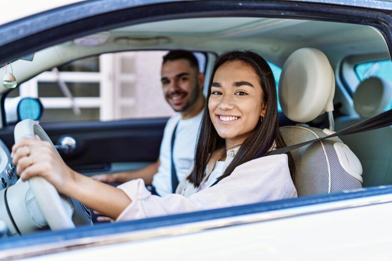 Woman smiling at the wheel of a car with a man smiling in the passenger seat.