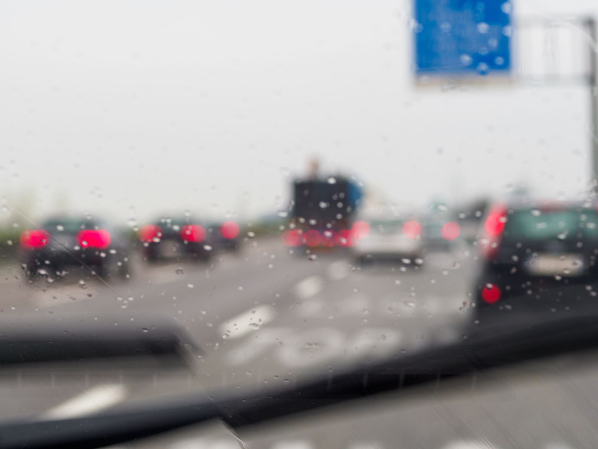 Traffic on a wet highway; blurry view through a windshield with rain droplets.