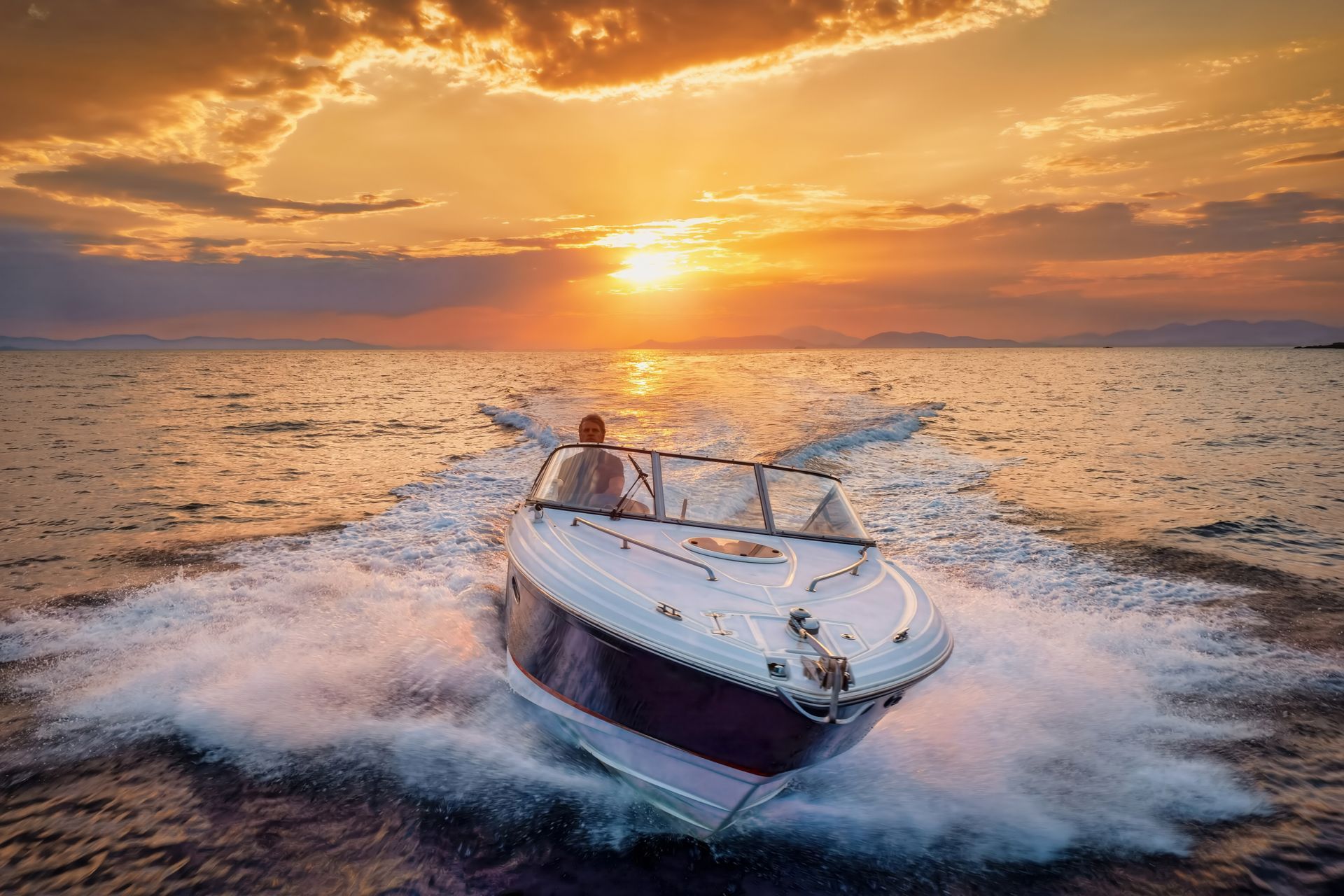 A motorboat cuts through open water toward a glowing sunset on the horizon, creating a large, white wake.