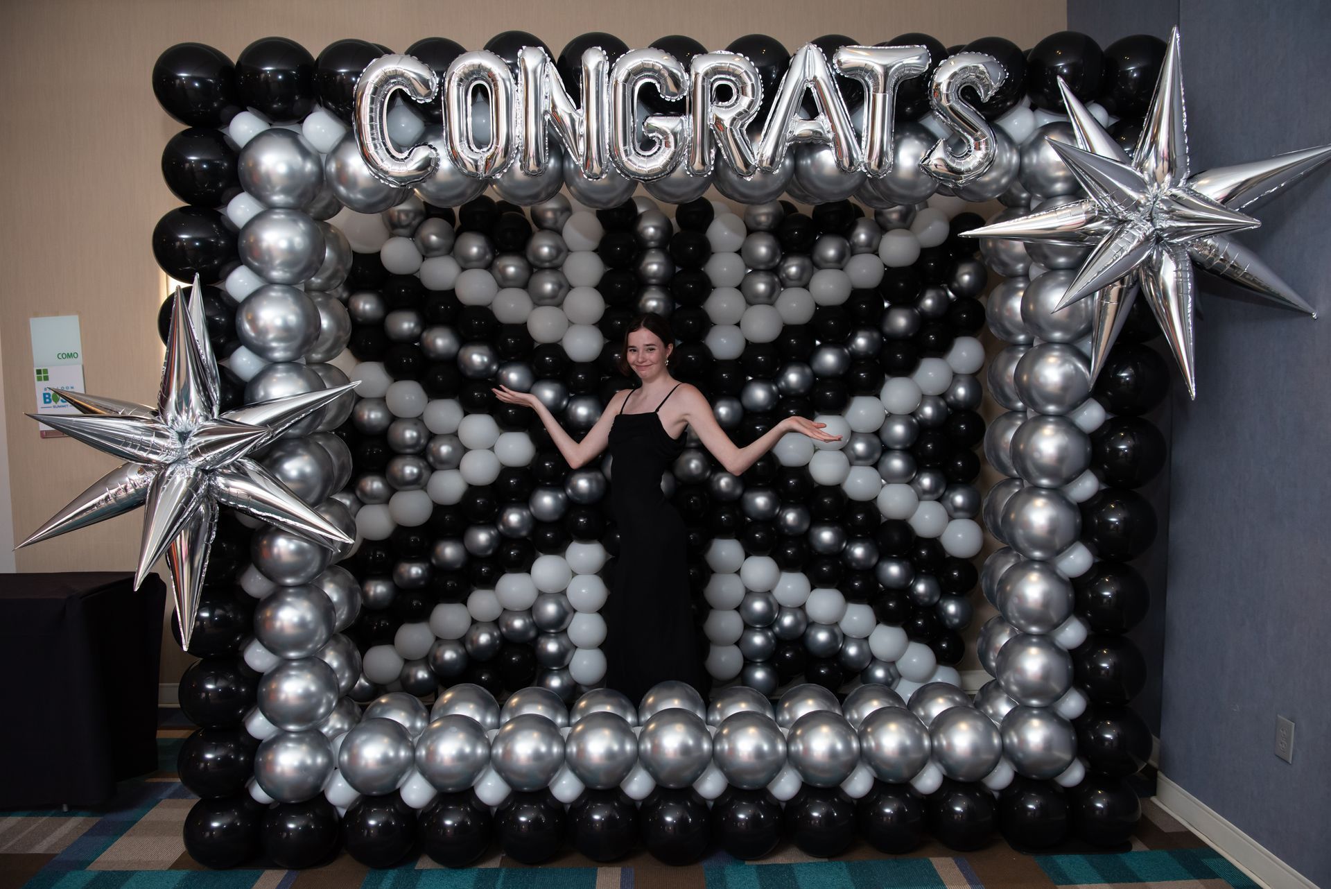 Woman poses in front of a balloon backdrop that spells