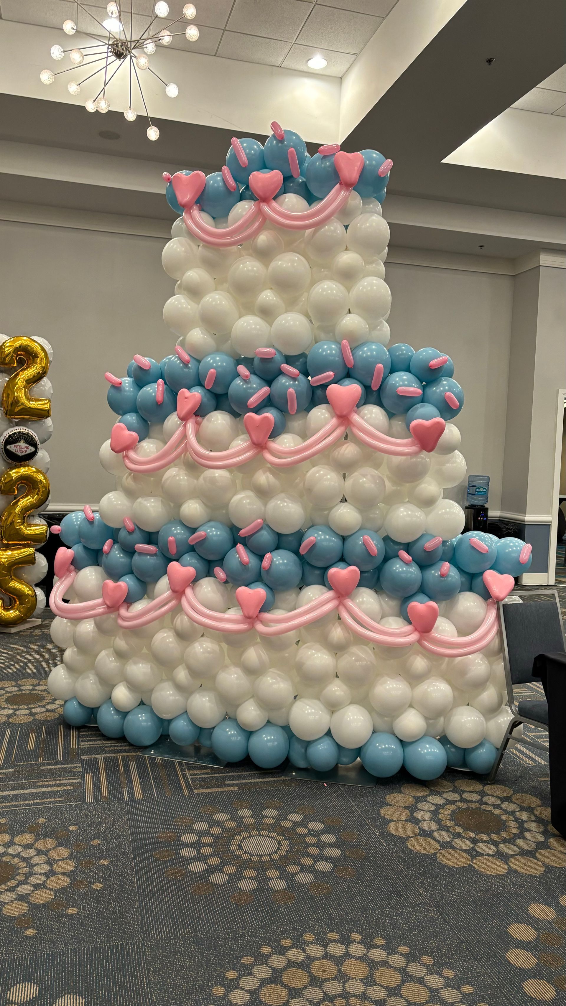 Three-tiered balloon cake decoration with white, blue, and pink balloons.
