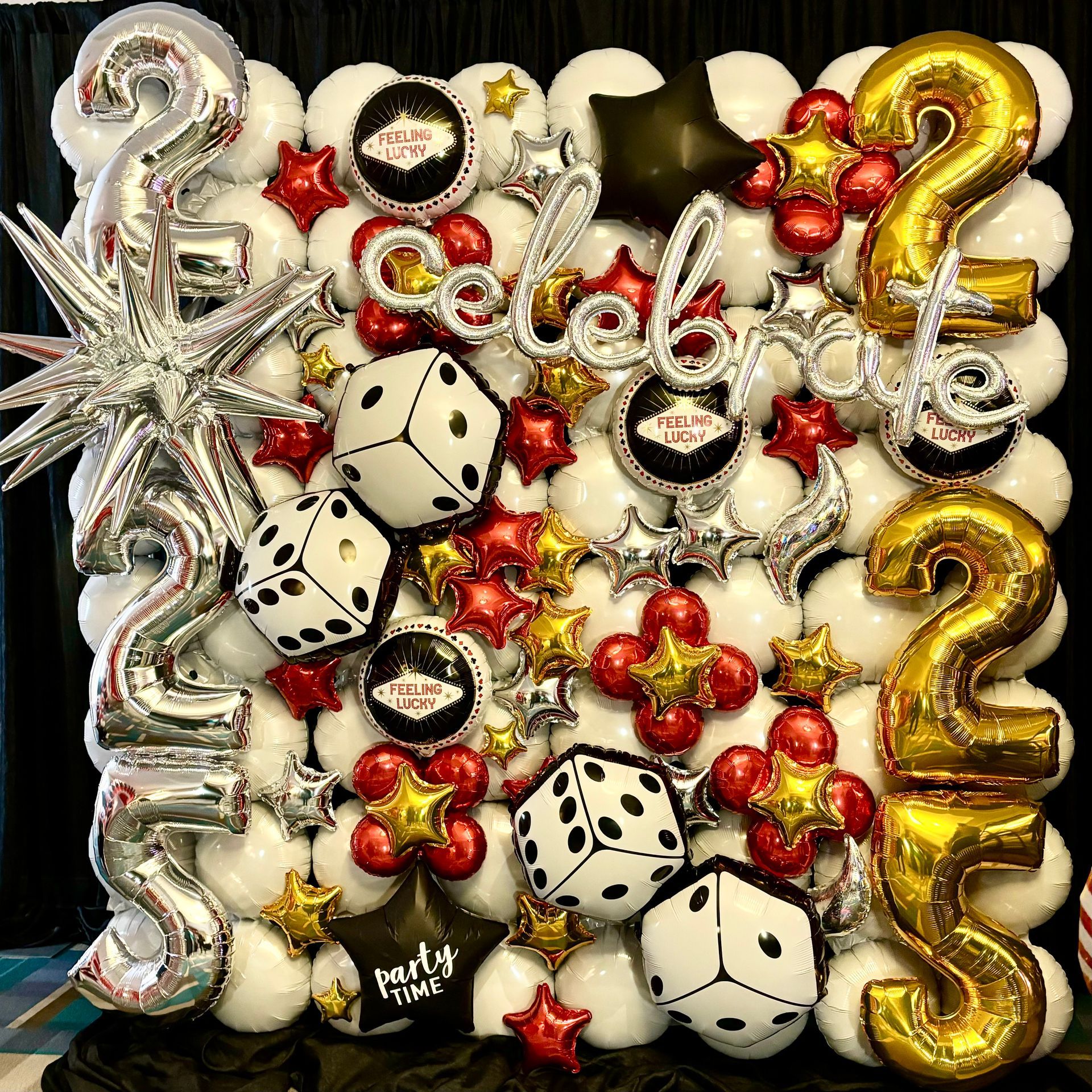 Casino-themed balloon wall with white, red, gold, and silver balloons, dice, and Vegas logo.