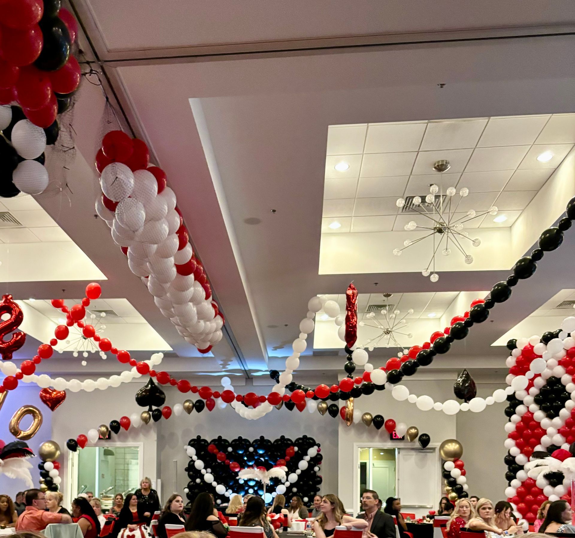 Party with red, white, black balloon decorations in a brightly lit room. People seated at tables.