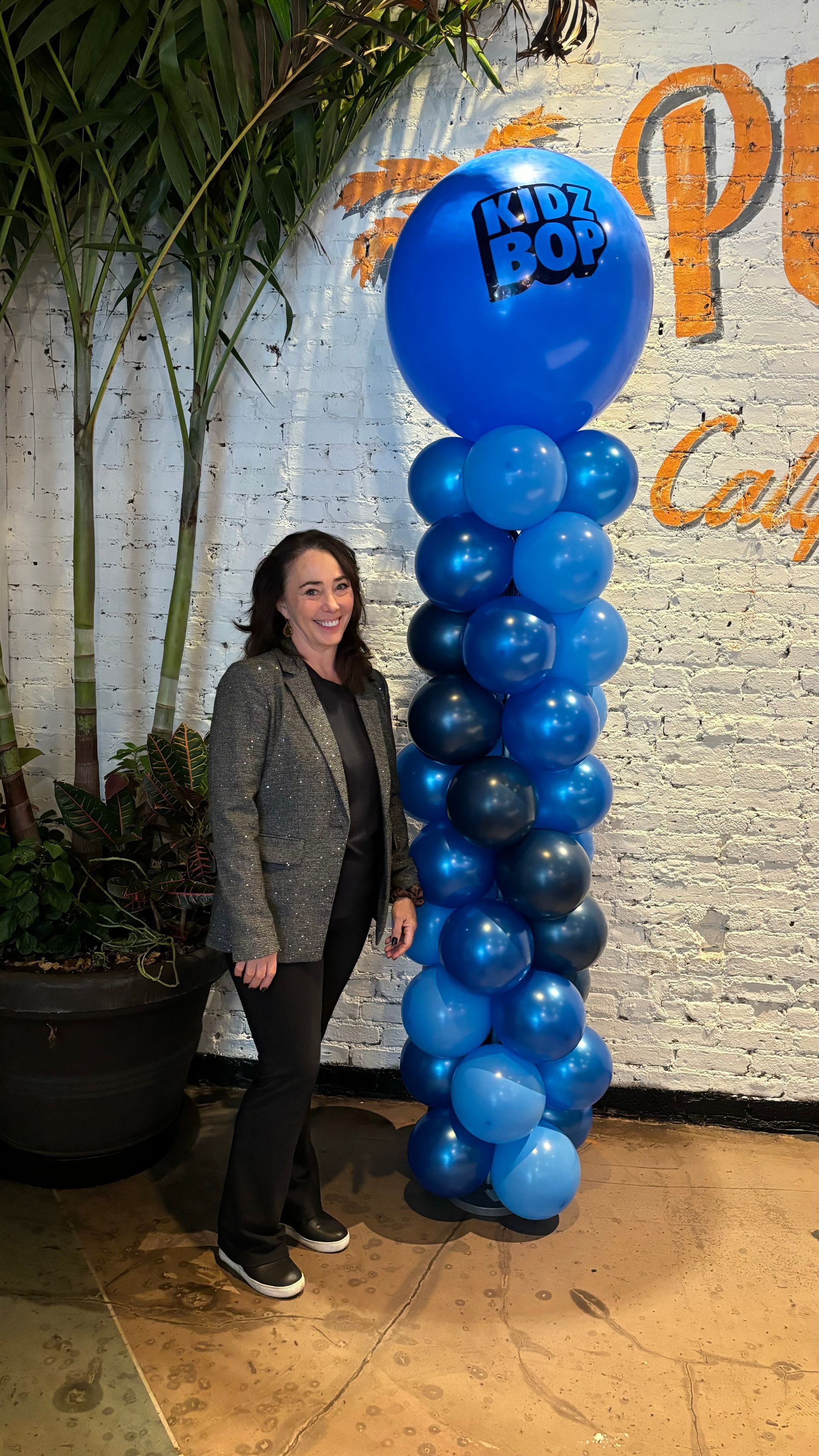 Woman stands next to a tall blue balloon column with a large top balloon, outside a venue.
