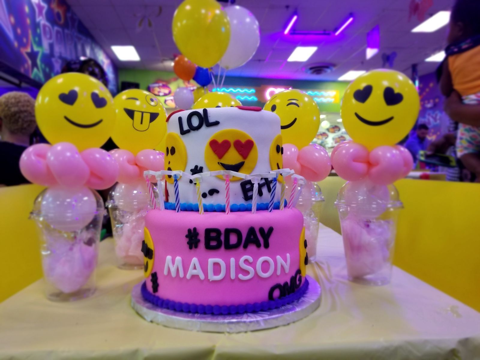 Birthday cake with emoji decorations and balloons. The cake is pink and has the name 