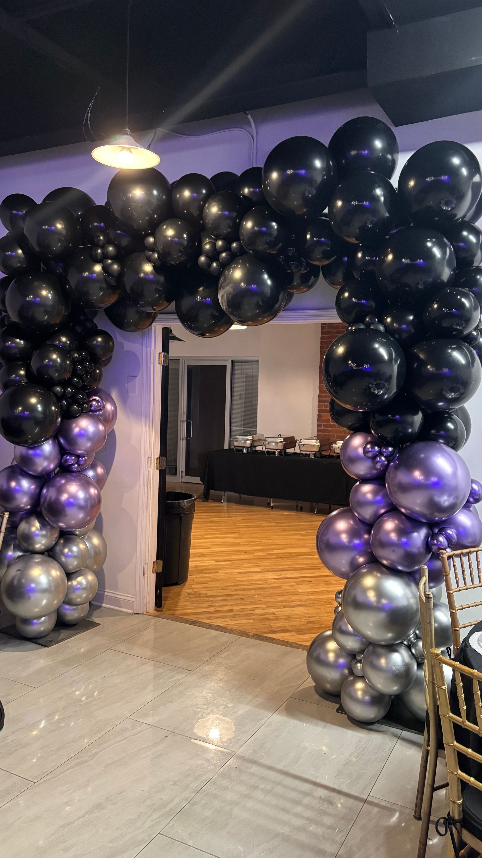 Black and silver balloon archway over an entryway, decorated for an event inside a building.