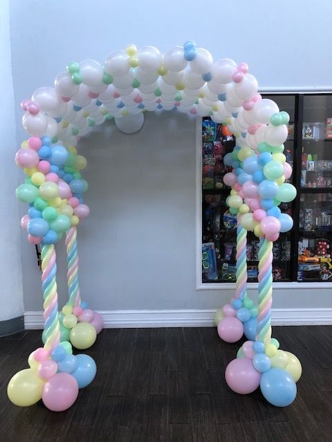 Balloon arch in pastel colors, featuring a rainbow design and a candy cane-like support structure.