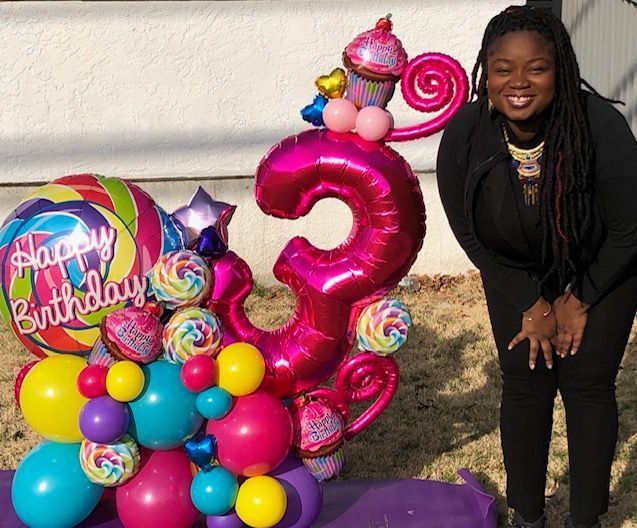 A woman is standing in front of a birthday balloon arrangement
