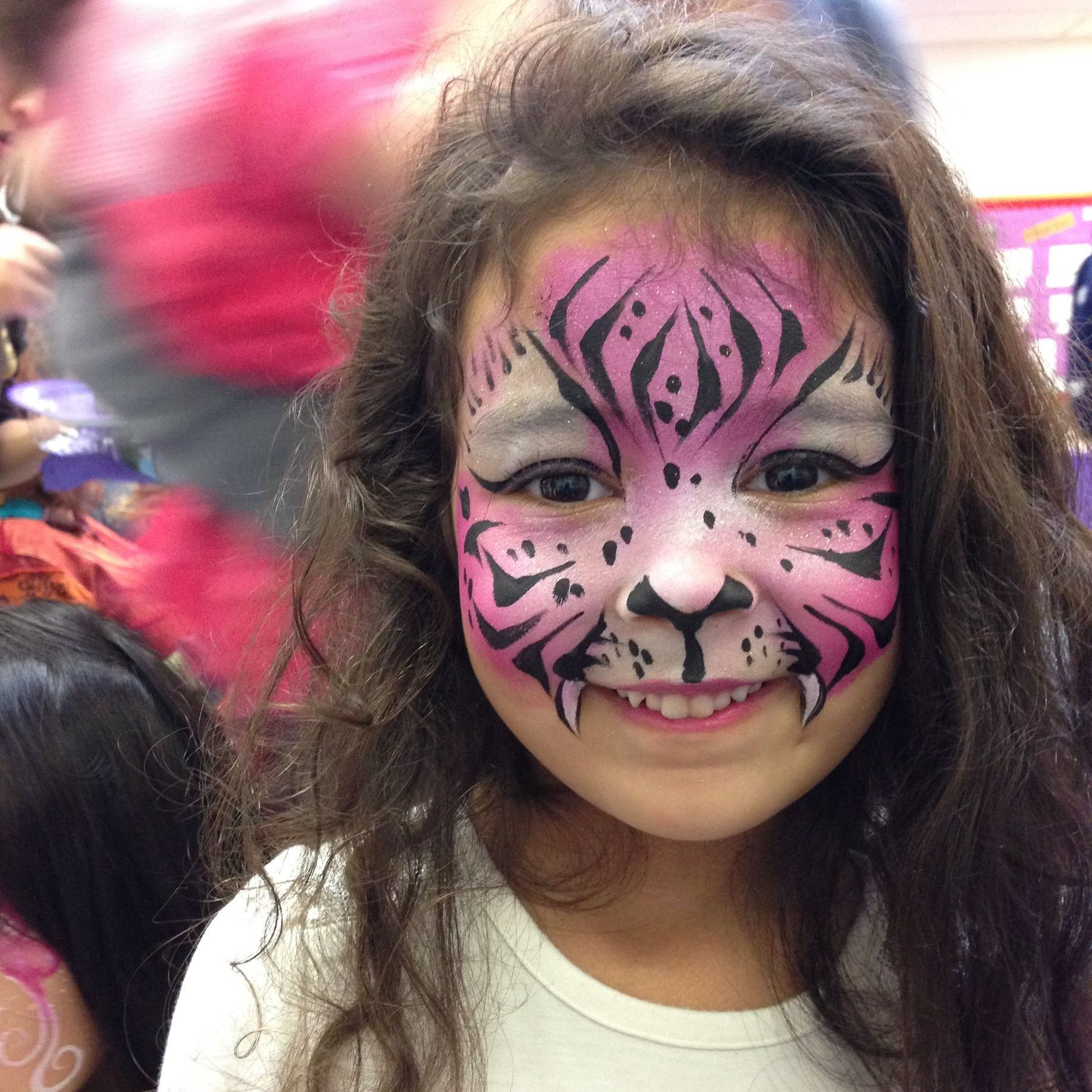 Girl with pink and black tiger face paint smiling.