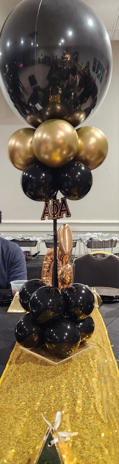 Black and gold balloon decoration on a table covered with gold fabric.