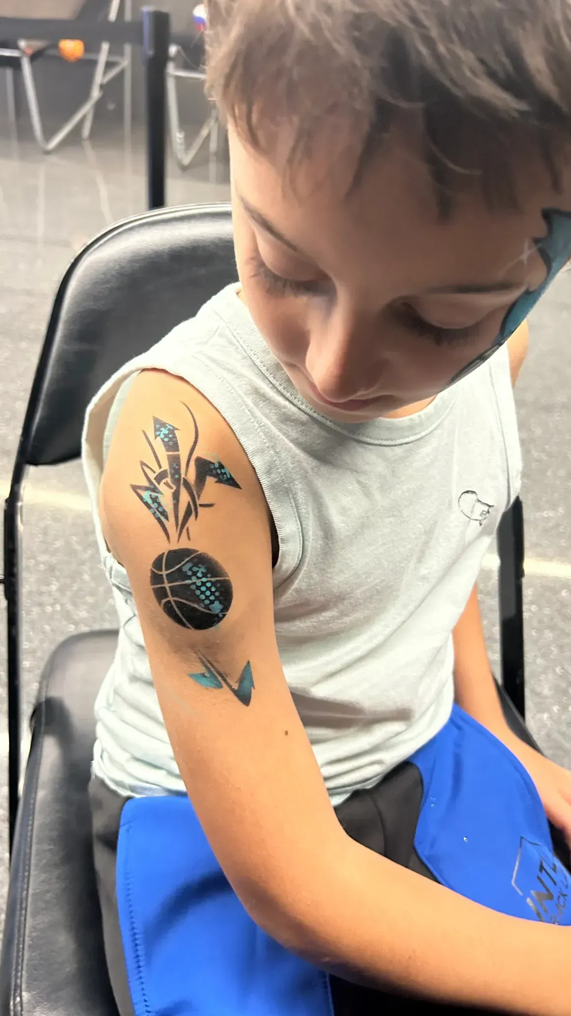 Boy with temporary arm tattoos sits in a chair, looking down at his arm.