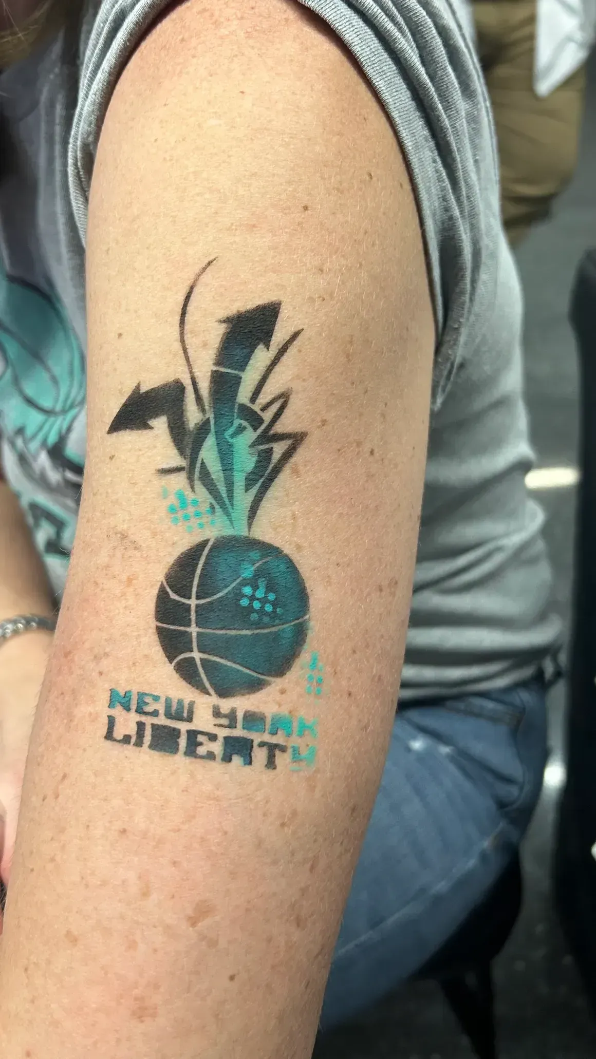 Tattoo of a teal basketball with black arrows and